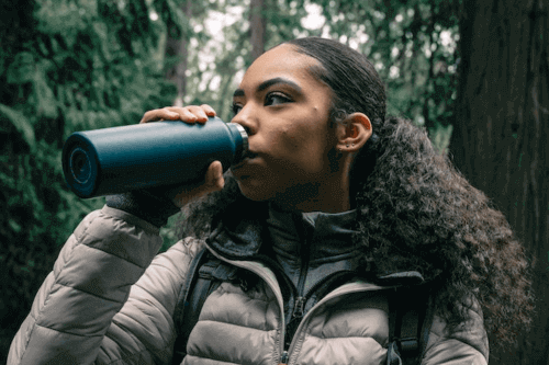 Best Water Bottles for Travel - Girl drinking in forest