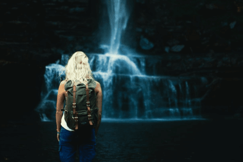 Woman with backpack standing near a waterfall