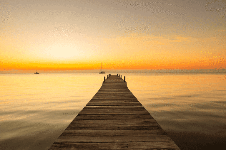 Wooden pier extending into sunset ocean